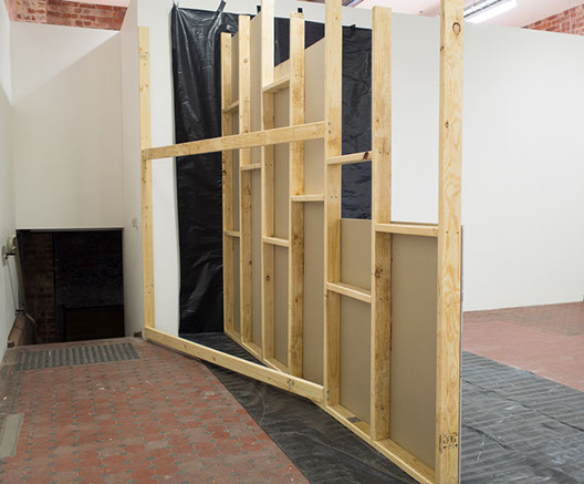 View of the back of the unfinished wall, timber scaffolding, dark passage way that looks like stairs going into another space.