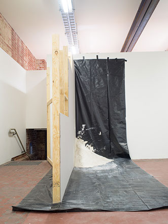 An unfinished constructed wall with tarp, a large plaster mound in the corner of the wall and tarp, appears set after being thrown in the corner