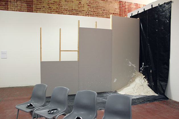 An unfinished constructed wall with tarp, a large plaster mound in the corner of the wall and tarp, appears set after being thrown in the corner