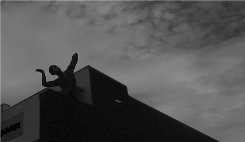 Black and White photo of a buildings roof and a silhouette of a sculpture looking toward the sky.
