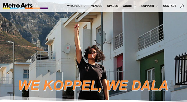 Metro Arts We Koppel We Dala Website Banner Image with orange text We Koppel We Dala on a photo of woman standing below housing with one fist raised high wearing all black.