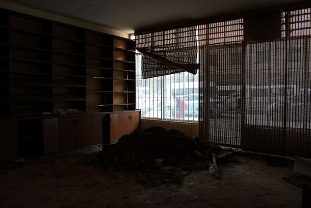 Artist documentation showing inside of a dark demolition site. Pile of dirt near closed bllind shutters with window showing busy traffic pass.