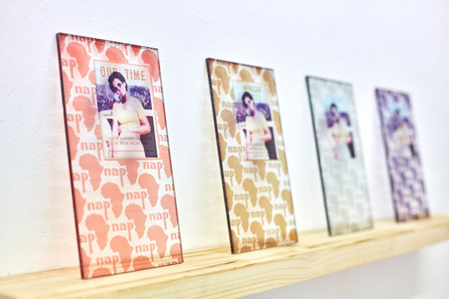 Prints on 4 perspex panels of Africa continent silhoettes, text and an African woman repeated on all, sits on a pine shelf against a white wall.